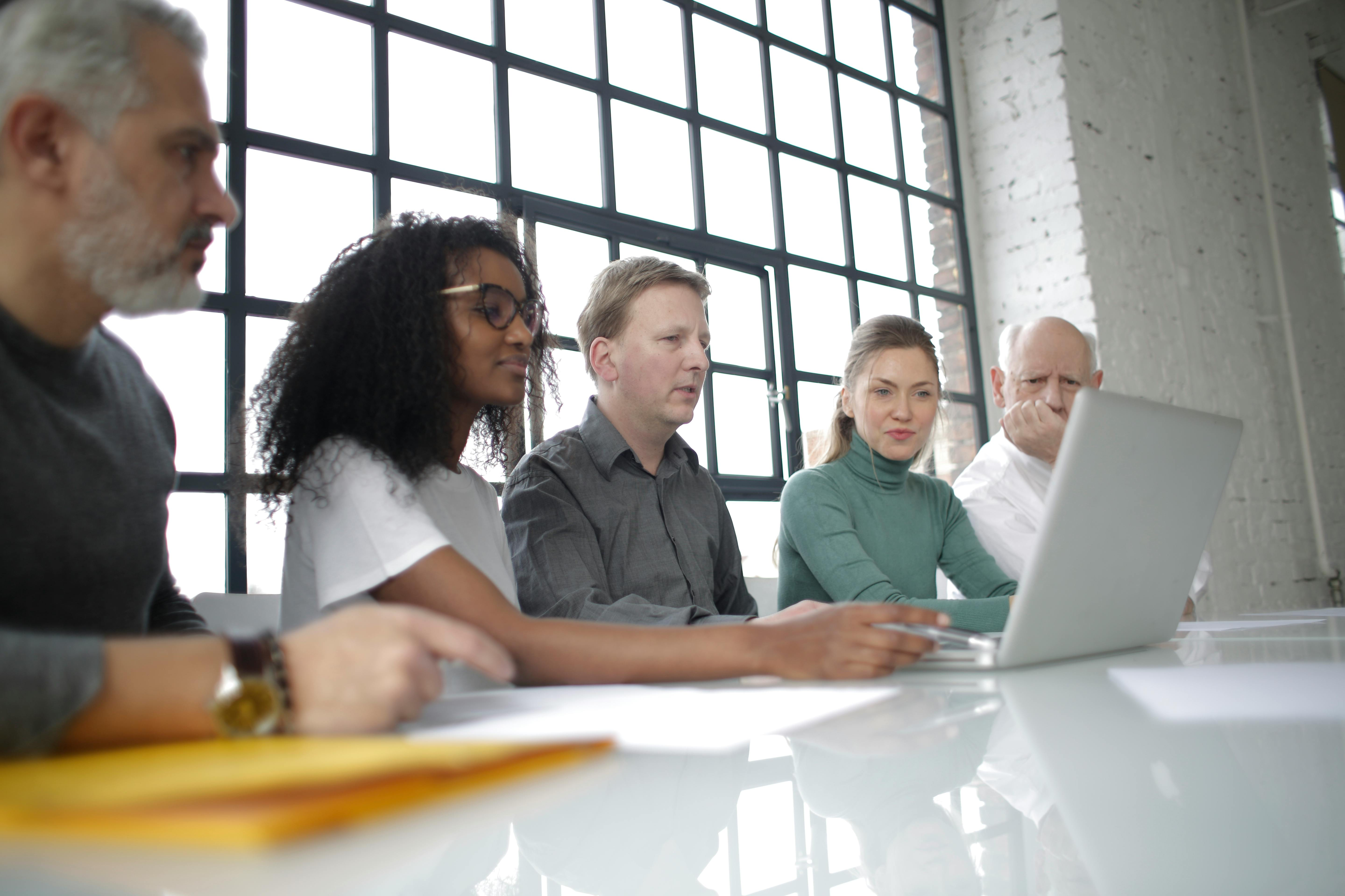 A business team gathered around a laptop in a bright office, representing shared team software purchasing and rollout